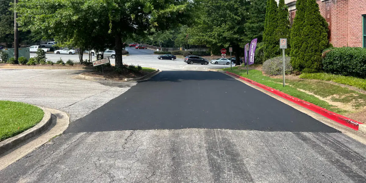 Fresh black asphalt overlay running away from the camera across a commercial drive, meeting the worn grey pavement it was laid over